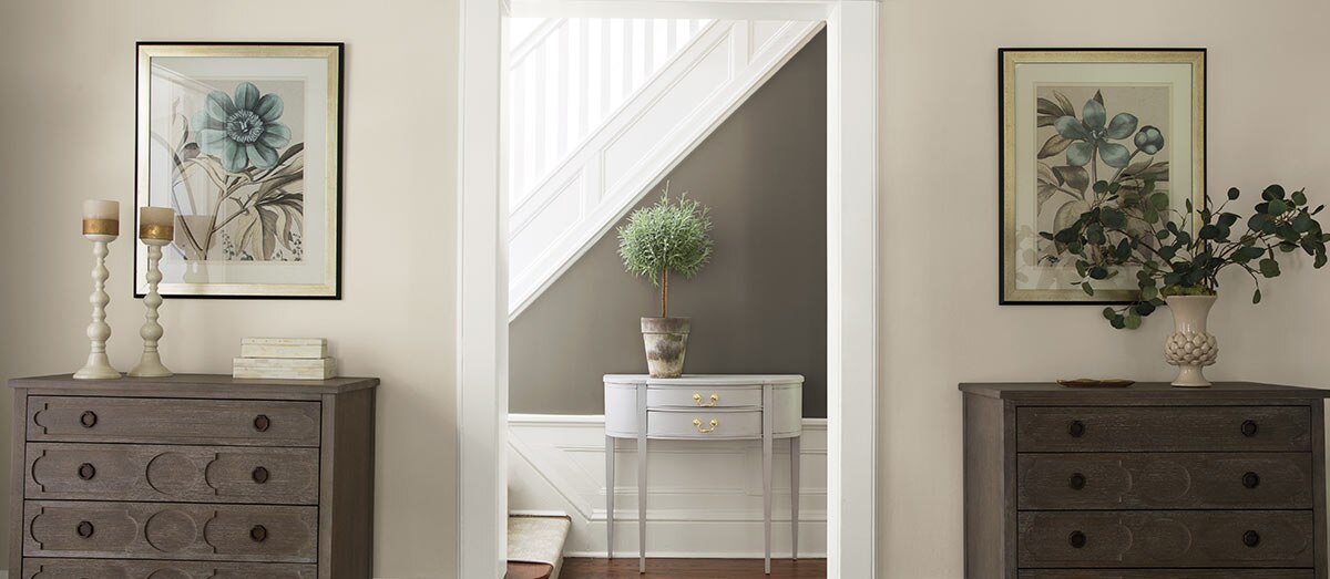 A gray hallway with white staircase and wainscoting includes a delicate console table and lustrous hardwood floors. A gray hallway with white staircase and wainscoting includes a delicate console table and lustrous hardwood floors.